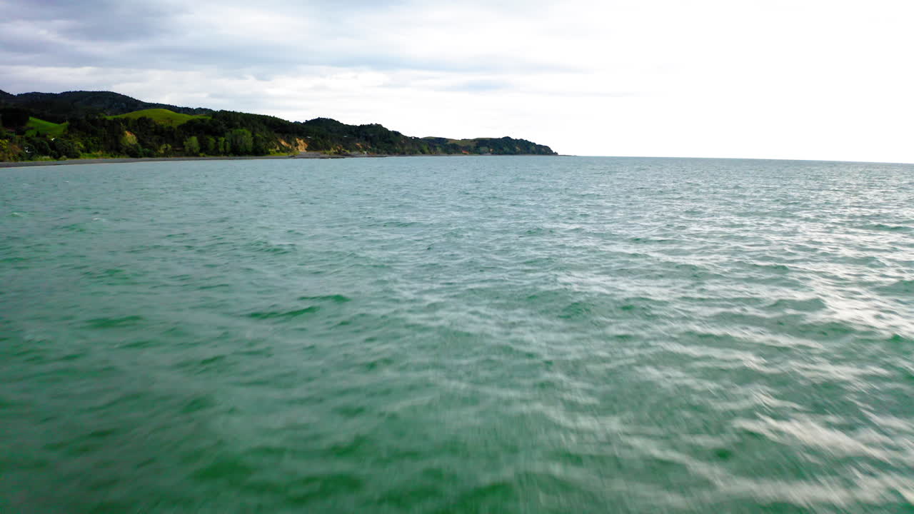 Coastal landscape with ocean and tree-lined hills under a cloudy sky