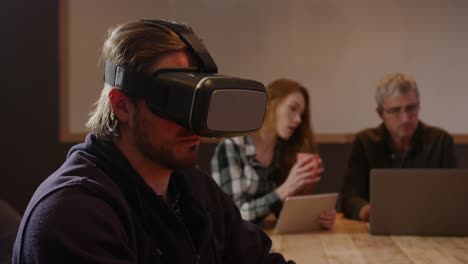 Man-wearing-VR-headset-with-colleagues-working-in-creative-office