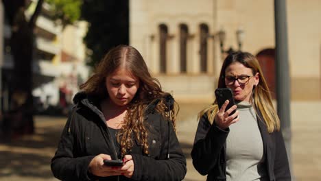 Two Women Walking on a City Street, Engaged with Their Smartphones