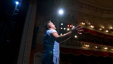 showman entertains the audience under the light, side view. big stage. serious performer speaks from the stage with streched hands.