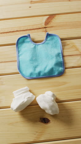 vertical video of close up of white booties and blue bib on wooden background with copy space