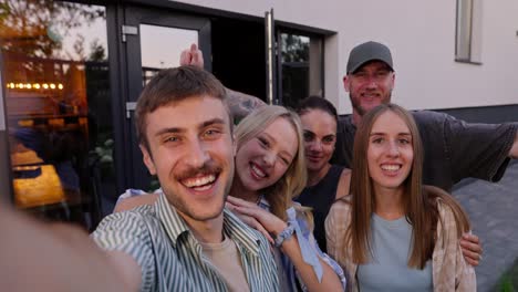 un alegre chico rubio toma una selfie con sus amigos divirtiéndose y posando en el patio de una casa de campo durante sus vacaciones