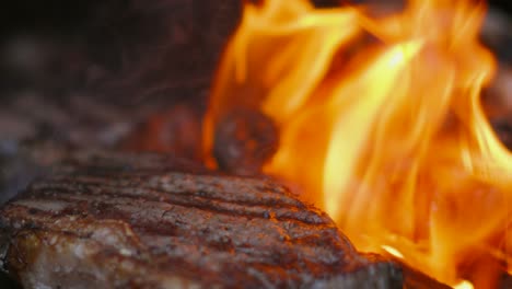 moving shot over flaming hot bbq cooking british beef sirloin steak with sausages in background in slow motion getting ready to serve to guests 4k