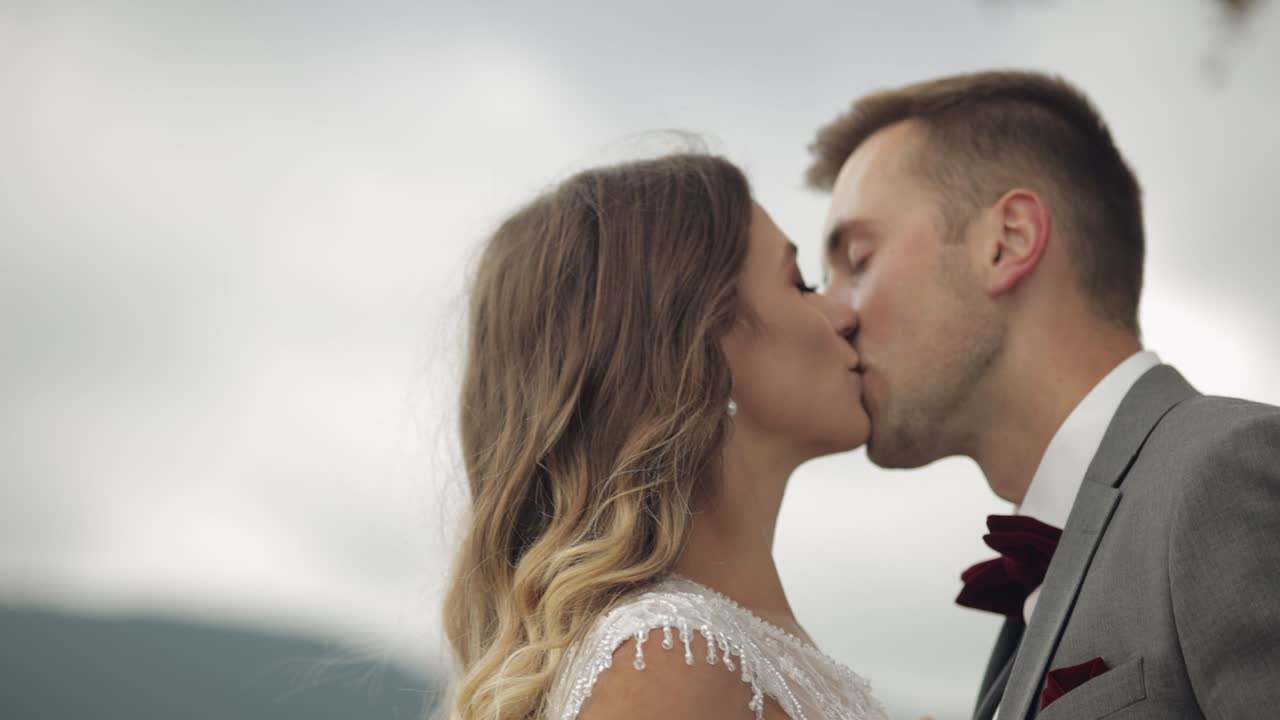 Adorabili sposi caucasici, famiglia, sposa e sposo che si tengono per mano, che si baciano su un pendio di montagna