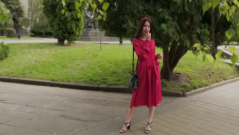 hermosa chica en rojo pinta labios con lápiz labial cerca de los árboles