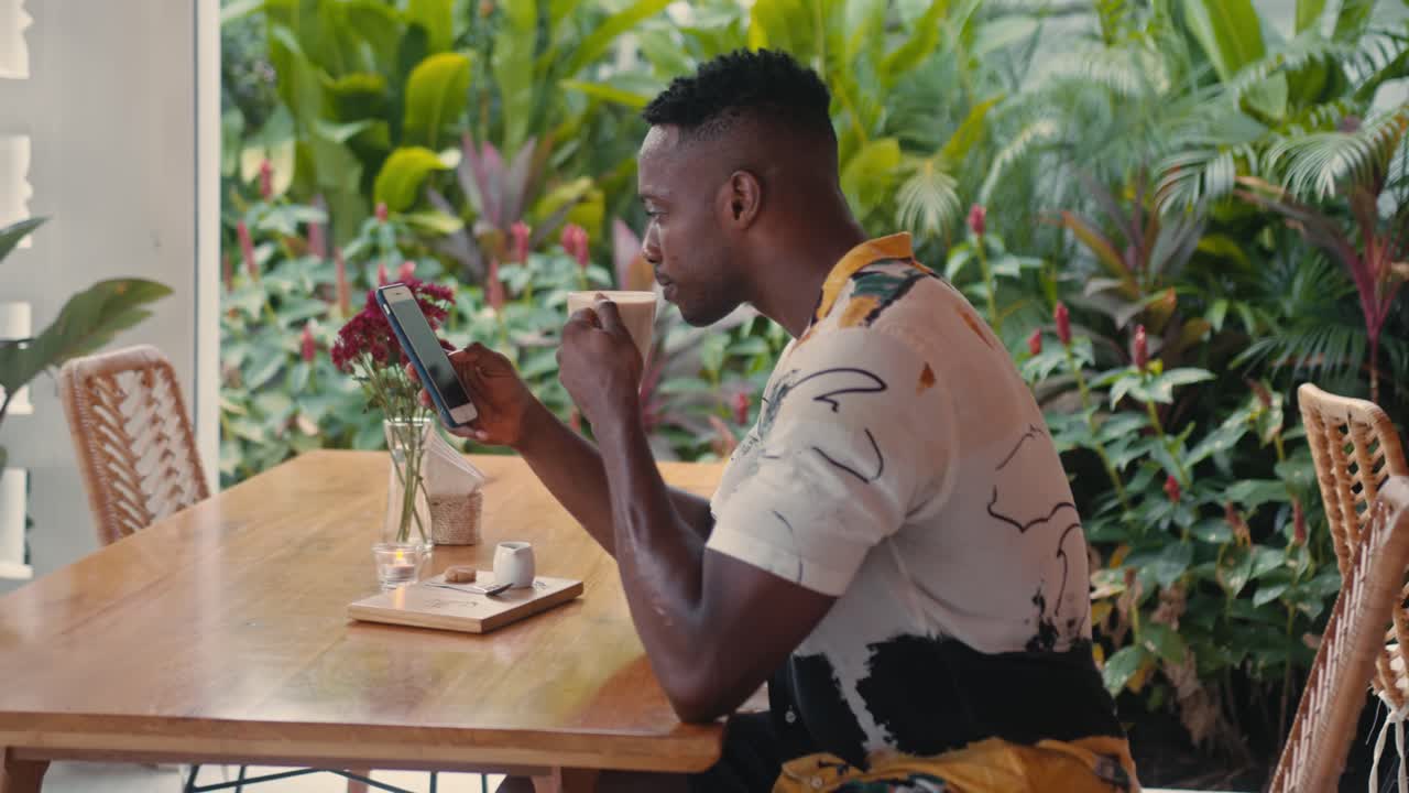Man Using Smartphone and Drinking Coffee at a Cafe
