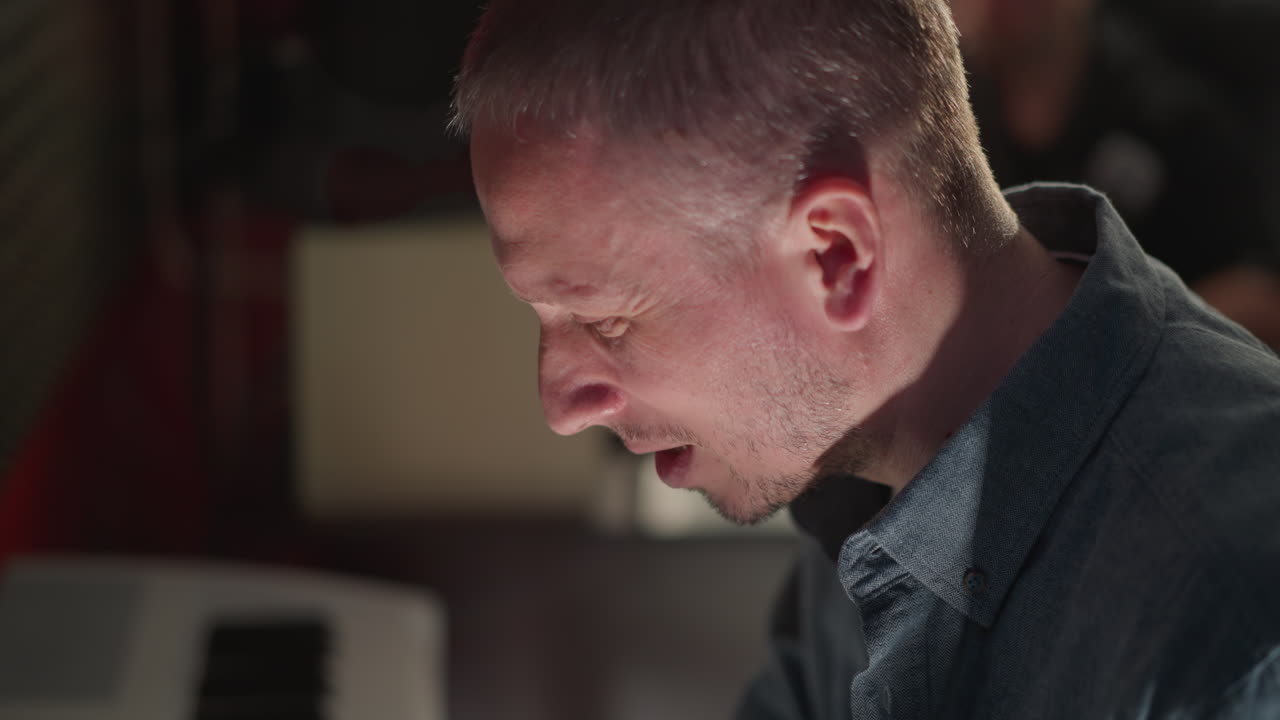 Close-up of a man in a blue shirt, appearing to play a piano with focus and concentration. The background is blurred, emphasizing the subject and creating a mood of creativity and musical engagement