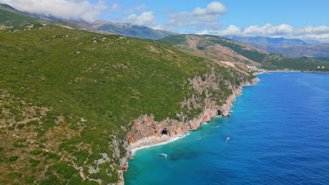 avión no tripulado en movimiento hacia atrás disparado volando alto sobre la playa de gjipe con cuevas visibles en la distancia en dharmi, albania en un día soleado