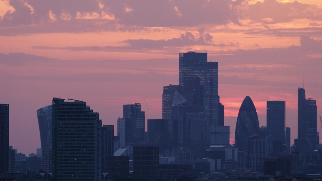 Medium telephoto panorama of London's skyline, highlighting the Gherkin, 22 Bishopsgate and surrounding skyscrapers against a colorful sunset.