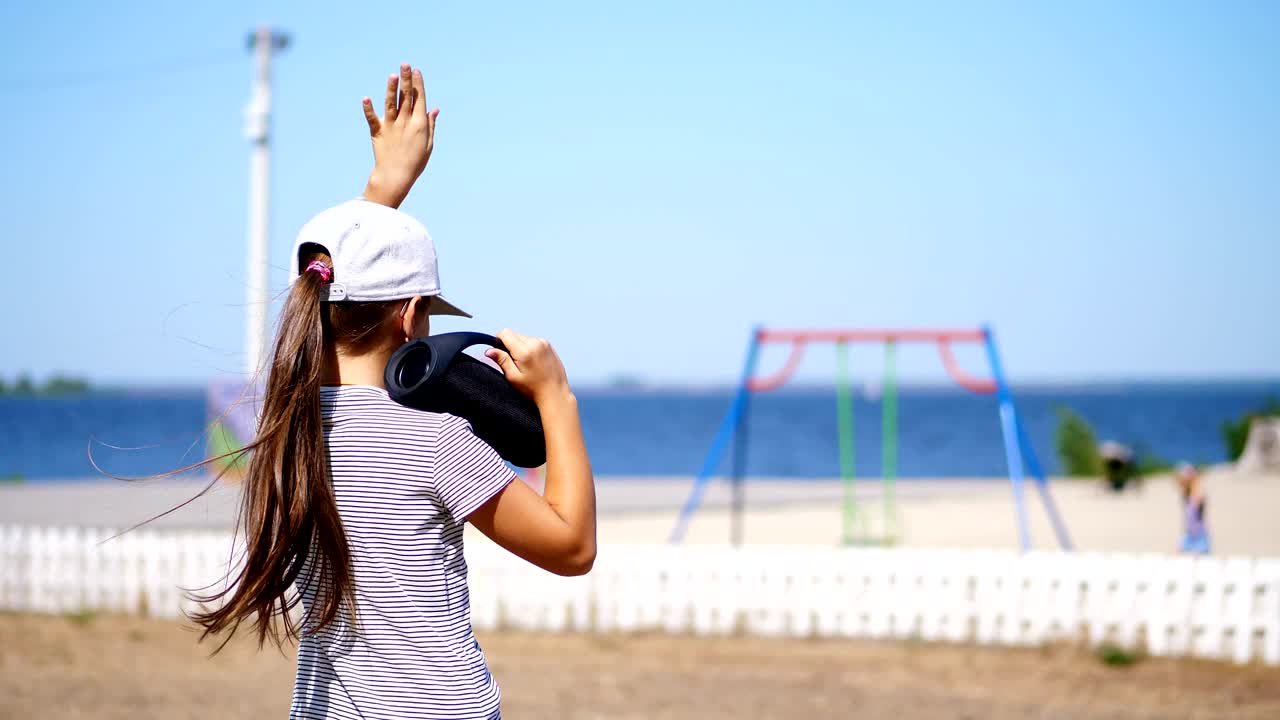 뒷면, 십대 아이, 블레이저를 입은 긴 머리 금발 소녀 블루투스 휴대용 스피커로 음악을 듣고, 해변에서, 춤을 추고, 뜨거운 여름 날