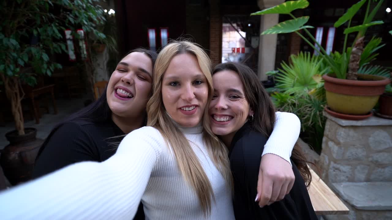 amigas alegres abrazándose mientras se toman una selfie en el bar