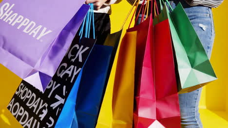 people holding various colorful shopping bags against a yellow background