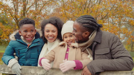 Portrait-of-smiling-family-with-parents-with-children-leaning-on-gate-on-walk-through-autumn-countryside-together---shot-in-slow-motion