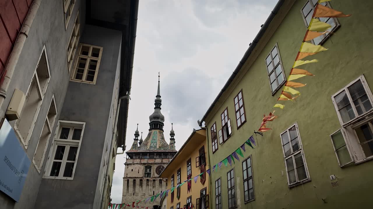 Medieval street with flag bunting below Sighisoara clock tower landmark