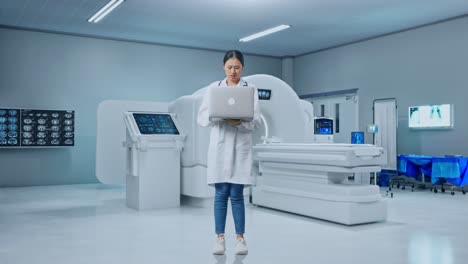 full body of tired asian woman doctor with stethoscope while working on a laptop with mri machine in the hospital