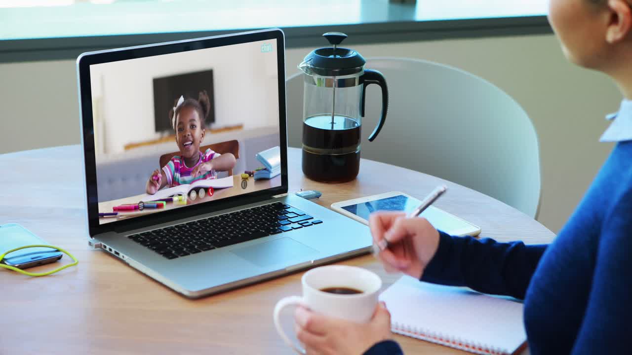 Caucasian female teacher drinking coffee and taking notes while having a video call on laptop