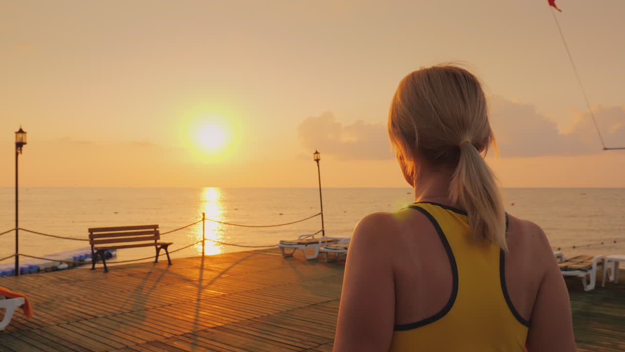 바다의 아름다운 일출을 배경으로 부두에서 몸을 녹이는 중년 여성