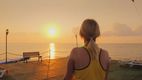 Frau-Mittleren-Alters,-Die-Sich-Auf-Dem-Pier-Vor-Dem-Hintergrund-Eines-Wunderschönen-Sonnenaufgangs-Am-Meer-Aufwärmt