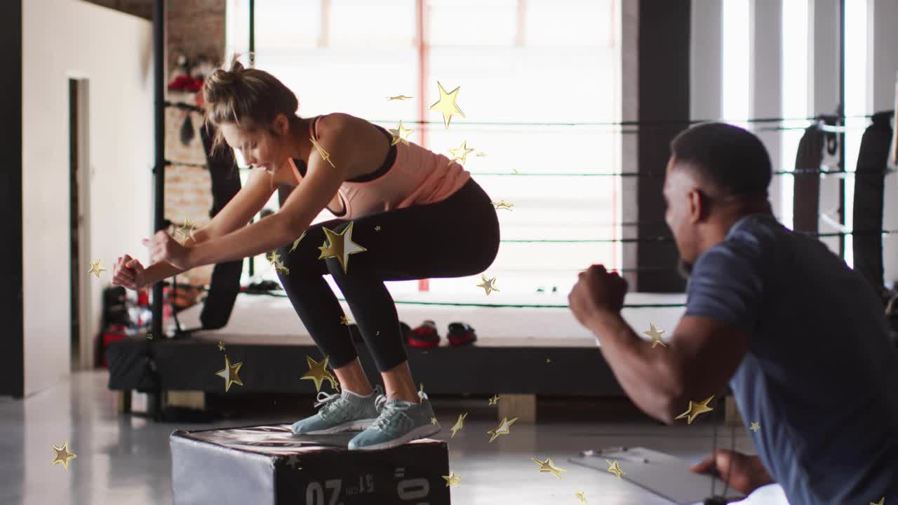 Female trainee squatting and jumping onto plyo box in gym as coach holding stopwatch recording jump