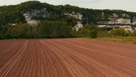 Lufttransportwagen,-Frisch-Gesätes-Erdfeld-Am-Fuße-Eines-Felsigen-Tals,-Sauber-Gemusterte-Traktorlinien