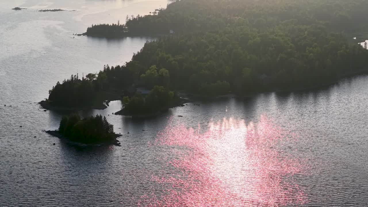 Aerial drone view of the sun reflecting pink light on the water around small forested islands in Michigan’s Upper Peninsula, Les Cheneaux Islands