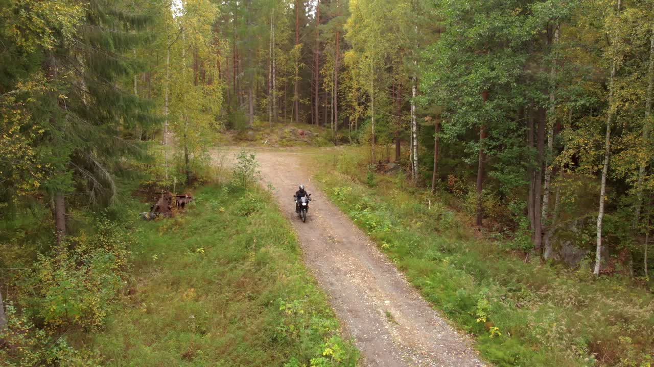 Motorcyclist driving towards the camera on a small gravel road in the forest