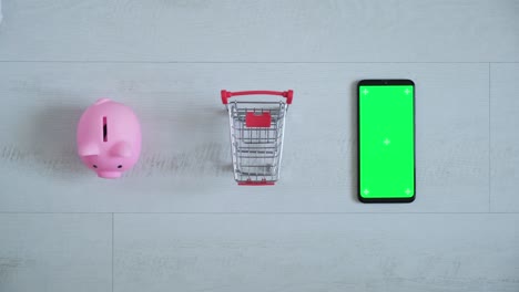 teléfono con una pantalla chromakey en las manos de un primer plano. vista superior de la caja de ahorros del teléfono inteligente y el carrito de compras copia el espacio sobre fondo blanco