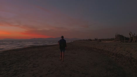 one young man walking on sandy beach at sunset