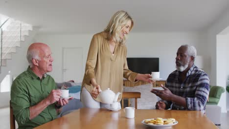 Zwei-Unterschiedliche-Seniorenpaare-Sitzen-Zu-Hause-An-Einem-Tisch-Und-Trinken-Gemeinsam-Tee