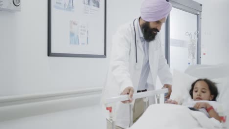 happy biracial doctor talking to sick girl patient in hospital bed in slow motion