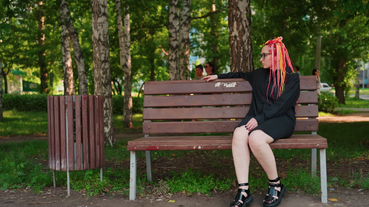 Женщина отдыхает на открытом воздухе: непринужденная поза, расслабленная женщина в парке, неспешно наблюдающая за окрестностями у дороги с деревьями; девушка с неоновыми косами наслаждается тишиной на городской скамейке