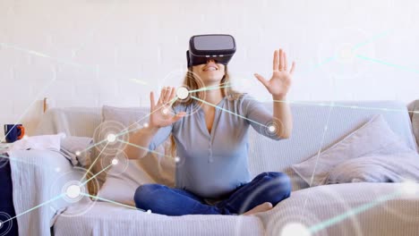 Animation-of-network-of-connections-with-icons-over-woman-wearing-vr-headset