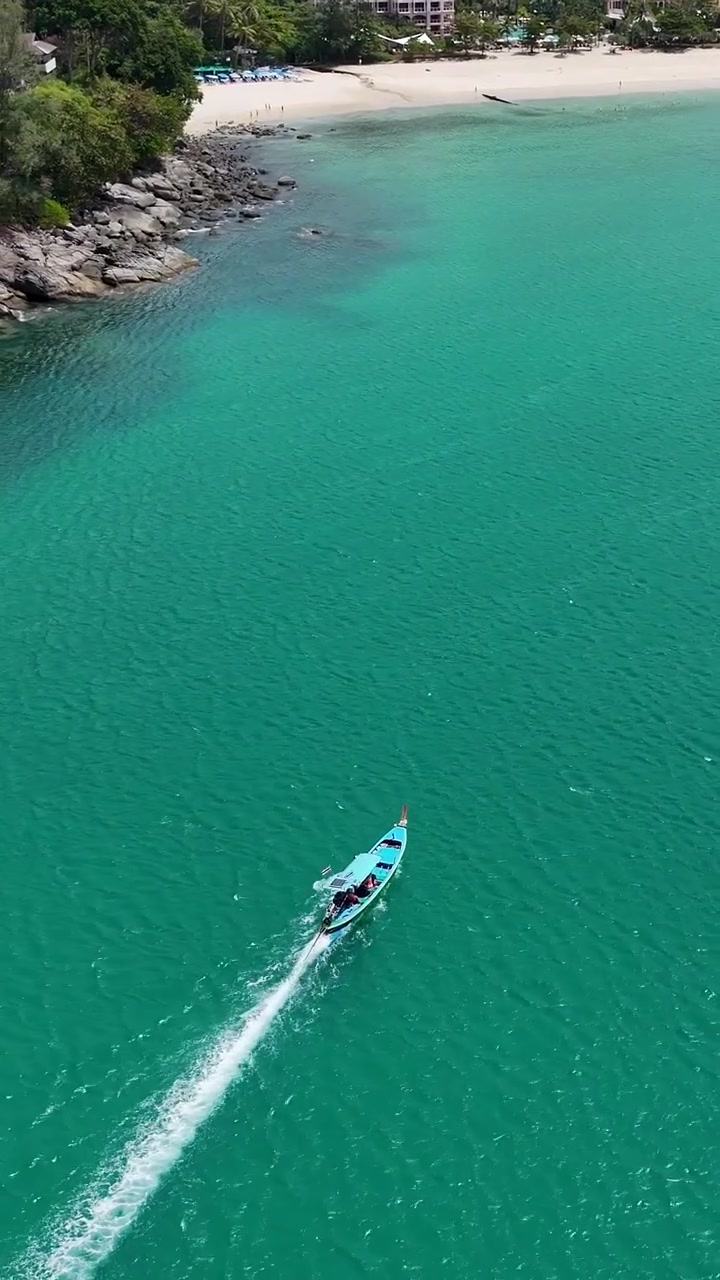 Veduta aerea di una barca che naviga lungo le acque turchesi vicino a Phuket, Thailandia, mettendo in mostra paesaggi costieri mozzafiato e i colori vivaci dell'oceano.