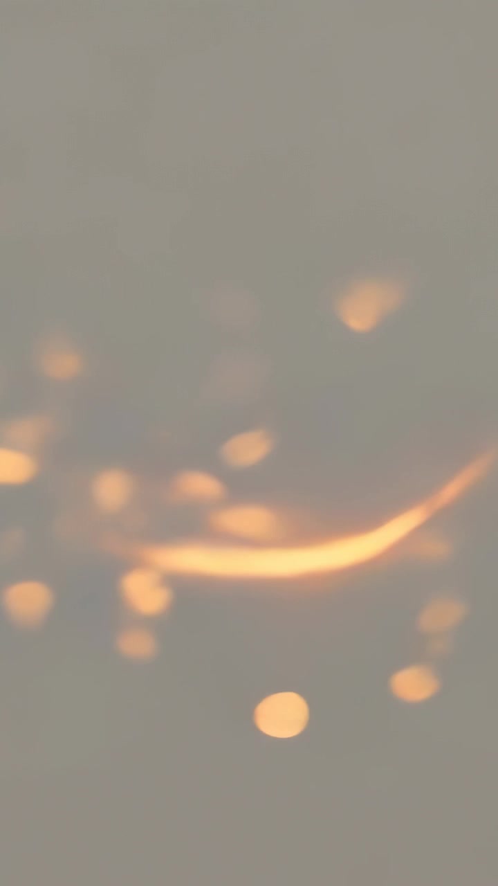Vertical video: Shifting focus causing warm bokeh moving across close-up gray field, curved streak