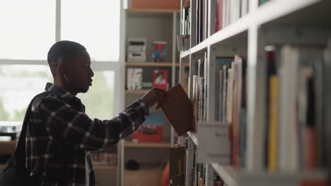 un hombre recoge un libro del estante de la biblioteca. un estudiante de piel oscura encuentra el libro correcto en el estante y va a leerlo. un tipo negro en la biblioteca estatal