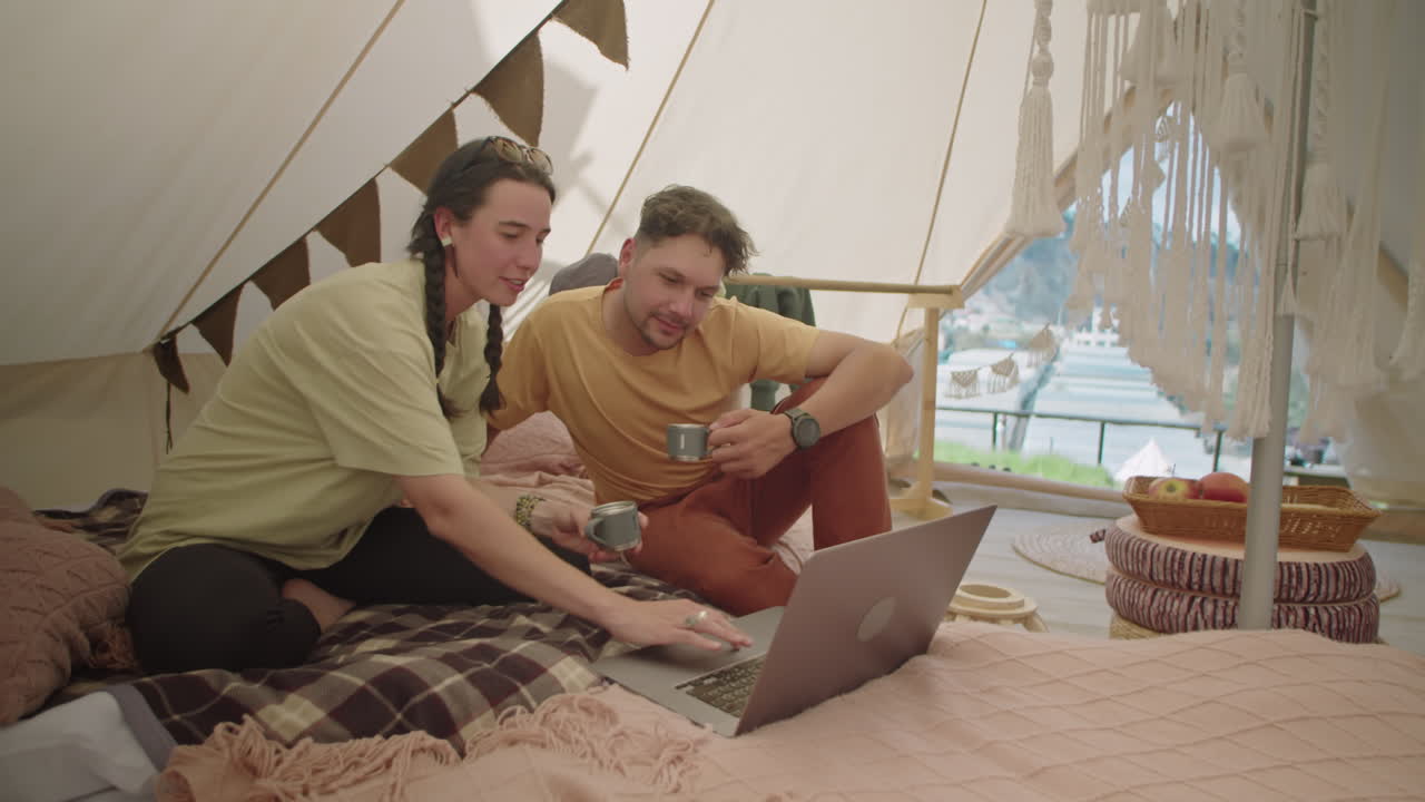 Couple Drinking Tea, Talking and Using Laptop in Glamping Tent