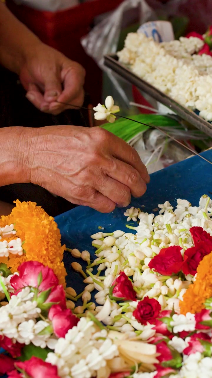 Primo piano di mani che infilano fiori freschi di gelsomino e calendula a Pak Khlong Talat, Thailandia