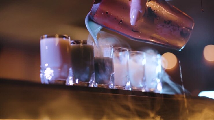 bicchierini da fumo con ghiaccio secco che si riempiono di cocktail colorati
