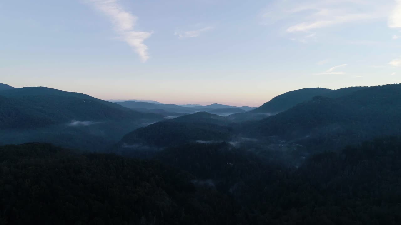Drone flying through mountain valley at sunrise.