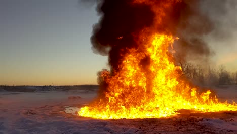 huge raging oil burning fire sends clouds of black smoke into the atmosphere as it melts the surrounding snow into a pool of water