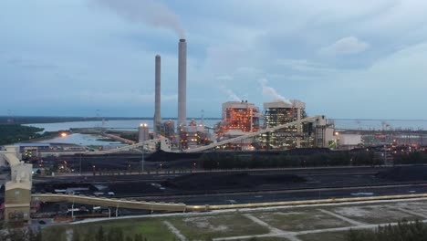 fly around the parameter of the coalfield and industrial ultra-supercritical coal-fired power plant with smokes raising from chimney located at costal area of manjung, perak, malaysia at dusk