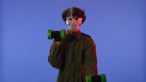 man in white mask swinging his arms with green dumbbells on blue background with red neon light