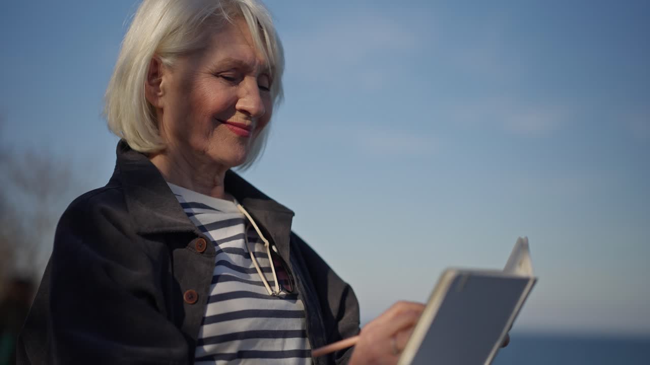 Senior Woman Drawing in Notebook by the Sea
