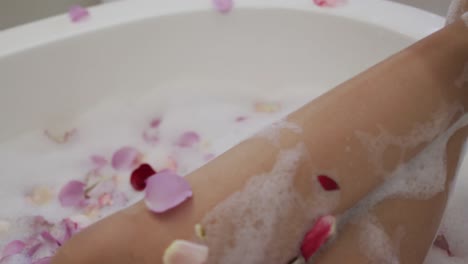 Mid-section-of-mixed-race-woman-taking-a-bath-with-rose-petals