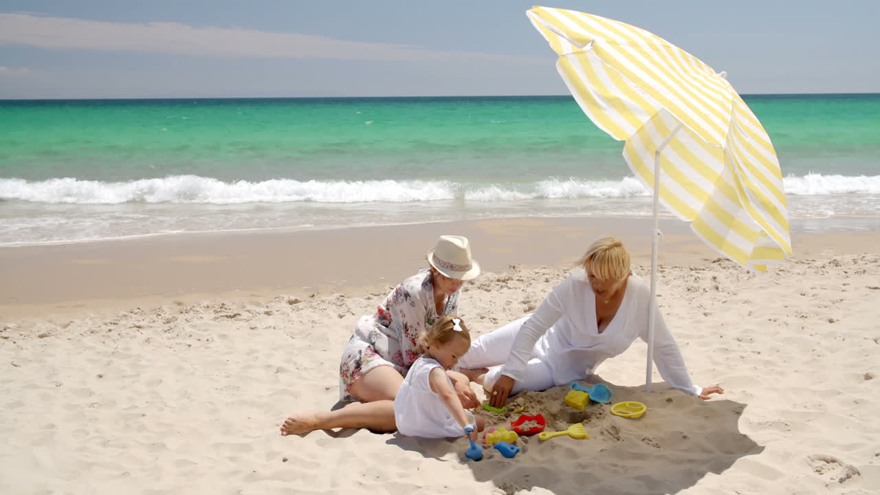 nonna, mamma e la bambina giocano sulla spiaggia.