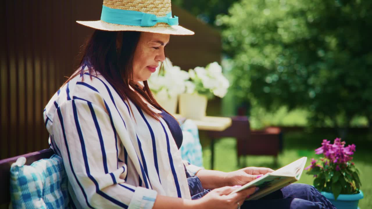 Woman in straw hat enjoying a book outdoors surrounded by greenery and vibrant flowers