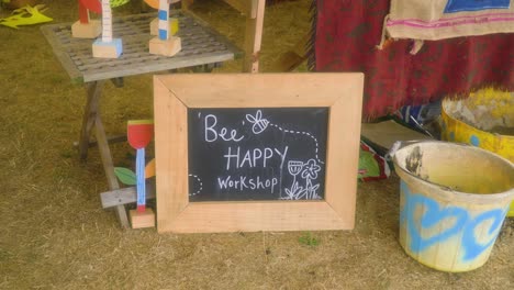 Bee-Happy-Workshop-Schild-Mit-Holzkohle-Auf-Dem-Boden-Im-Zelt-Platziert,-Damit-Kinder-Mit-Schlamm-Spielen-Und-Mit-Natürlichen-Werkzeugen-Und-Zutaten-Kreativ-Werden-Können