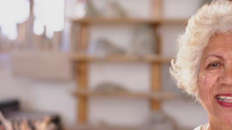 mitad de la cara de una mujer biracial con el cabello trenzado de pie y sonriendo en el estudio de cerámica, cámara lenta
