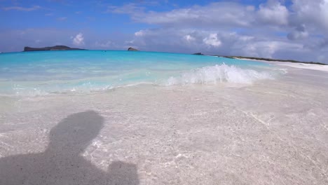 turquoise water and white sand beach of a paradisiac island of the galapagos islands. waves are crashing into the shore. some cruises and islands are seen on the back