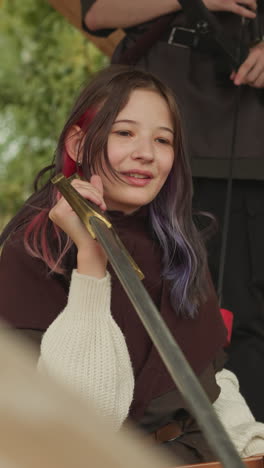 medieval warriors talk sitting in village yard. girl with sword smiles listening attentively. heroes rest after battle on blurred background closeup